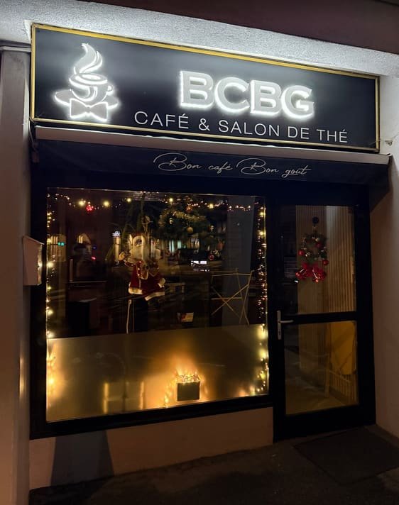 Devanture du BCBG Café le soir : enseigne lumineuse « BCBG, café & salon de thé » et lumière chaude à l’intérieur.